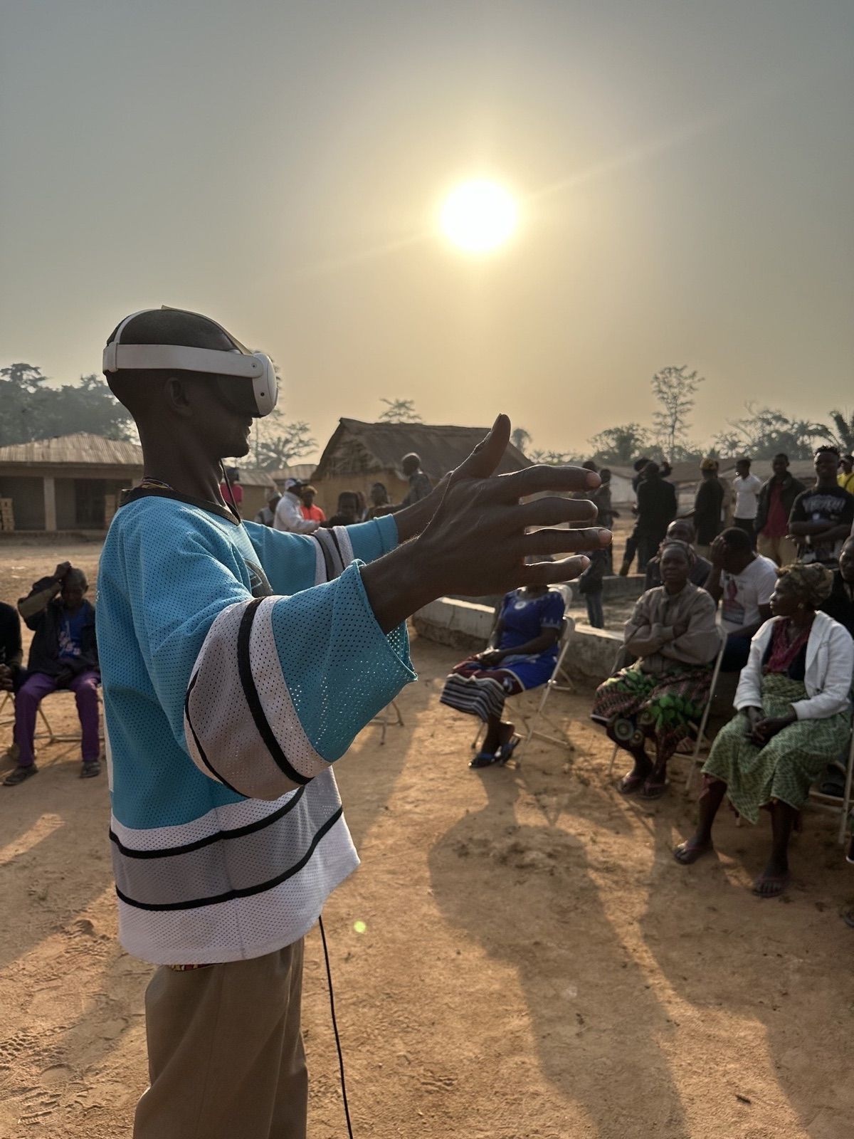 Arthur Saygbah wears a VR headset and reaches forward during an outdoor gathering in Selega, Liberia.